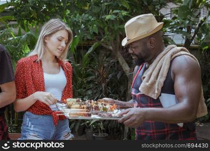Smiling chef give barbecue to friend for dinner camping in nature outdoor as summer lifestyle
