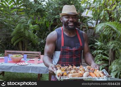 Smiling chef with barbecue dinner camping in nature outdoor as summer lifestyle