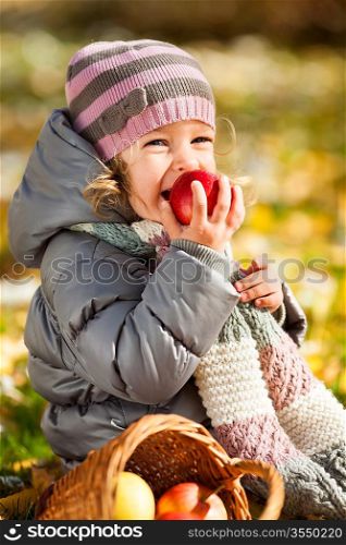 Smiling child eating red apple in autumn park. Healthy lifestyles concept