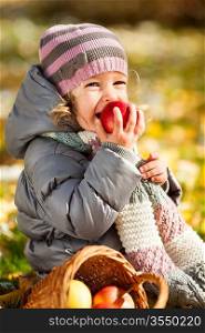 Smiling child eating red apple in autumn park. Healthy lifestyles concept