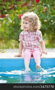 Smiling child sitting on border of swimming-pool in summer garden
