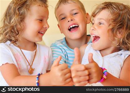 Smiling children three together in cosy room shows >: gesture