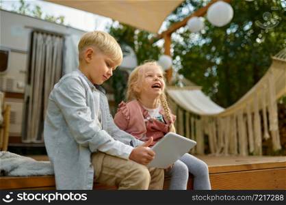 Smiling children using laptop at the trailer, summer camping. Family with kids travel in rv car. Campsite adventure, travelling lifestyle, vacation in motorhome. Smiling children using laptop at trailer, camping
