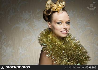 smiling christmas woman posing with freckles, glossy golden creative make-up, tinsel around neck and lovely ribbon on hair-style