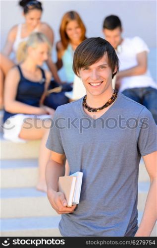 Smiling college student boy holding books friends in background summer