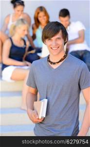 Smiling college student boy holding books friends in background summer