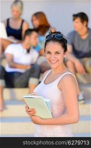 Smiling college student girl holding books friends in background summer