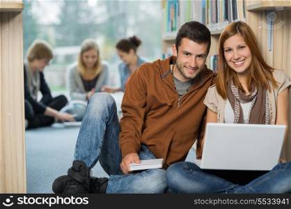 Smiling college students with laptop with classmates in library