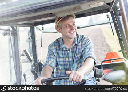 Smiling confident farmer driving tractor at farm