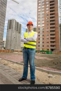 Smiling confident worker in helmet and safety vest standing on building site
