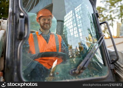 Smiling construction worker driving vehicle sitting in cab. Heavy equipment operator closeup shot. Construction worker in vehicle cab closeup shot