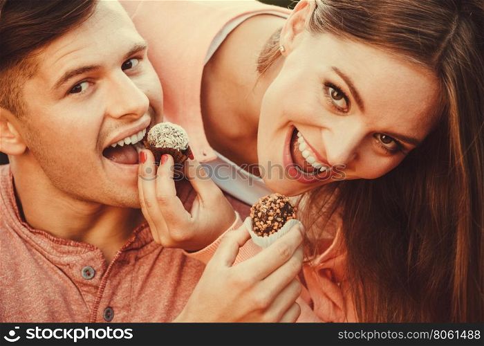 Smiling couple feeding each other.. Love and happiness. Cute lovely lovers feeding each other by cupcakes cookies. Smiling couple with sweet food having fun.