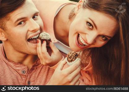 Smiling couple feeding each other.. Love and happiness. Cute lovely lovers feeding each other by cupcakes cookies. Smiling couple with sweet food having fun.