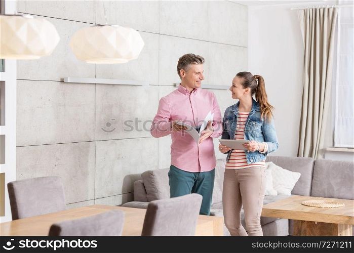 Smiling couple holding agreement papers while standing in apartment