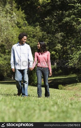 Smiling couple holding hands walking and talking in park.