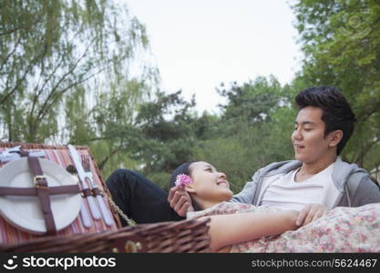 Smiling couple in love having a picnic in the park, lying down on the blanket with picnic basket open