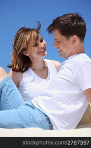 smiling couple in white shirts sitting on sand