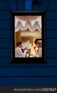 smiling couple is sitting at restaurant, view from street