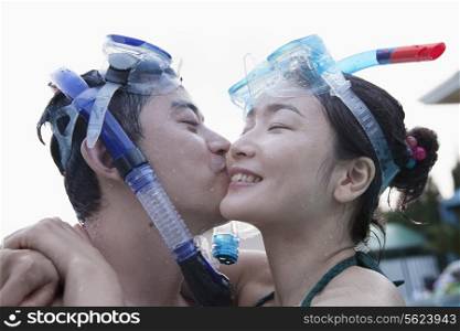 Smiling couple kissing on the cheek wearing snorkeling gear in the pool