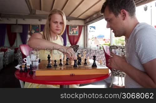 Smiling couple playing a game of chess while sitting at a table enjoying a drink