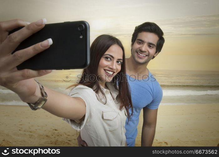 Smiling couple taking selfie on beach at sunset