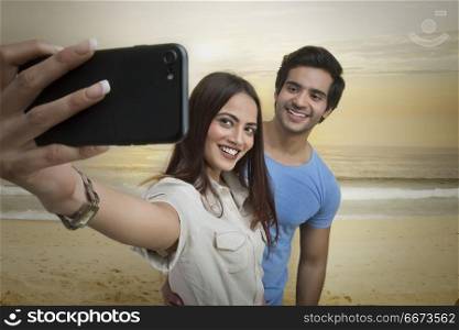 Smiling couple taking selfie on beach at sunset