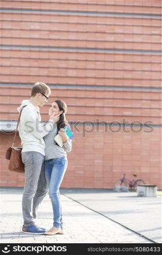 Smiling couple with books standing at university campus