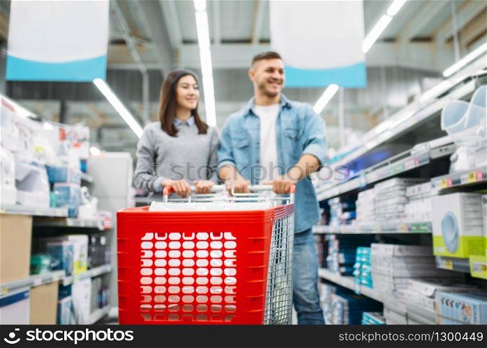 Smiling couple with trolley in market, family shopping. Customers in shop, buyers choosing consumer goods
