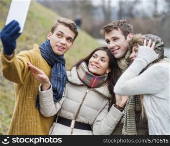 Smiling couples taking self portrait through cell phone in park
