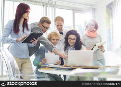 Smiling creative businesspeople working on laptop at desk in office