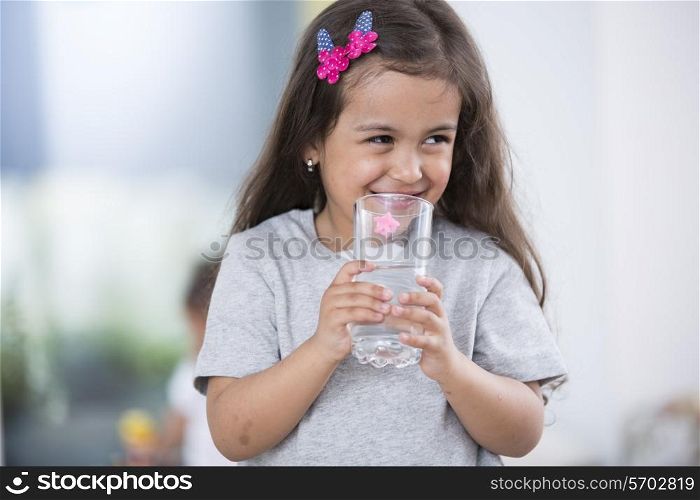 Smiling cute girl holding glass of water at home