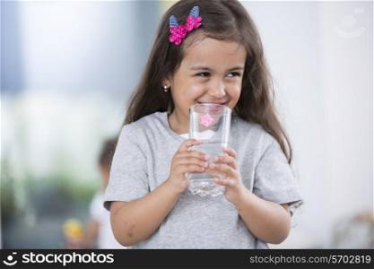 Smiling cute girl holding glass of water at home