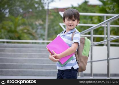 Smiling cute little boy with school backpack and holding book ready for first day of school