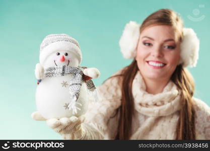 Smiling cute woman with little snowman. Winter.. Smiling pretty cute woman holding little snowman. Attractive girl in earmuffs and white sweater pullover in studio on green. Winter fashion.