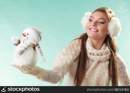 Smiling cute woman with little snowman. Winter.. Smiling pretty cute woman holding little snowman. Attractive girl in earmuffs and white sweater pullover in studio on green. Winter fashion.