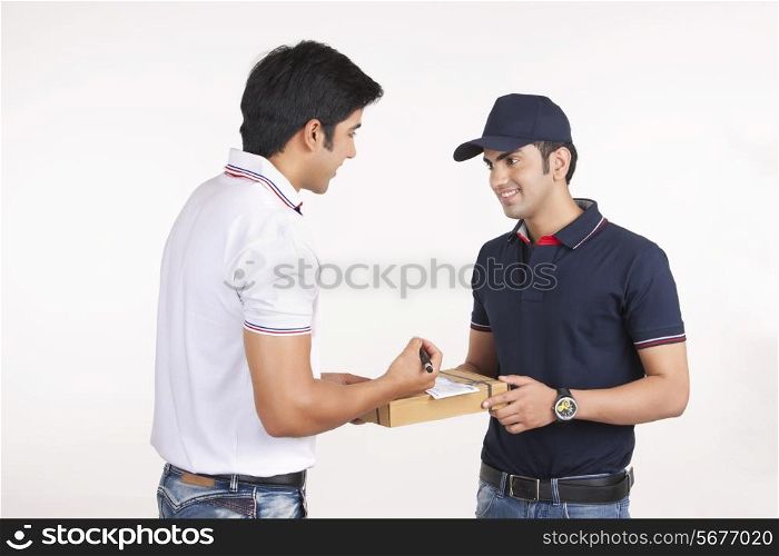 Smiling delivery man delivering package to customer against white background