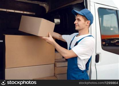 Smiling deliveryman with carton box at the car, delivery service. Man in uniform holding cardboard package, male deliver, courier job