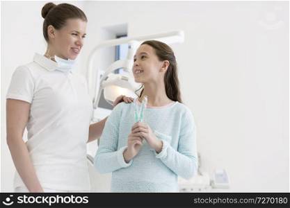 Smiling dentist and girl with toothbrushes at dental clinic