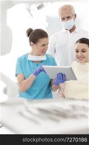 Smiling dentist discussing with patient over digital tablet at dental clinic