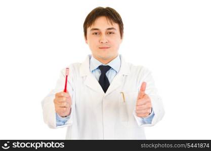 Smiling dentist holding toothbrush and showing thumbs up gesture isolated on white&#xA;