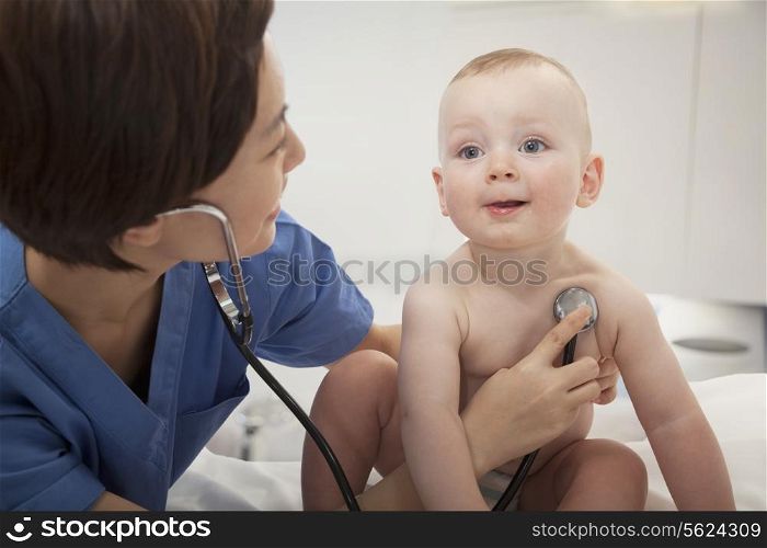 Smiling doctor checking a baby&rsquo;s heart beat with a stethoscope in the doctors office