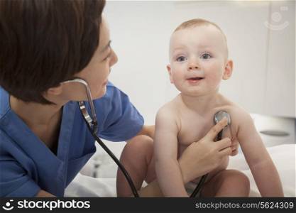 Smiling doctor checking a baby&rsquo;s heart beat with a stethoscope in the doctors office