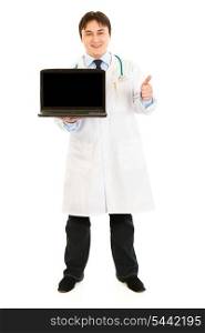 Smiling doctor holding laptops with blank screen and showing thumbs up gesture isolated on white&#xA;