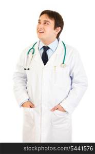 Smiling doctor with hands in pockets looking up at copy space isolated on white&#xA;