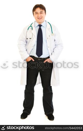 Smiling doctor with stethoscope keeping his hands in pockets isolated on white&#xA;