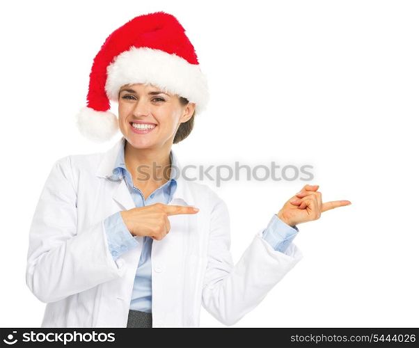 Smiling doctor woman in santa hat pointing on copy space