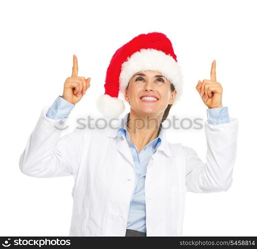Smiling doctor woman in santa hat pointing up on copy space
