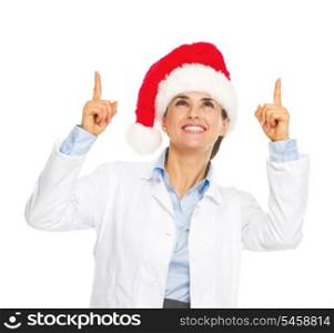 Smiling doctor woman in santa hat pointing up on copy space