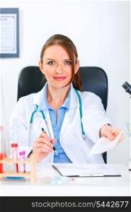 Smiling doctor woman sitting at office table and giving medical prescription&#xA;