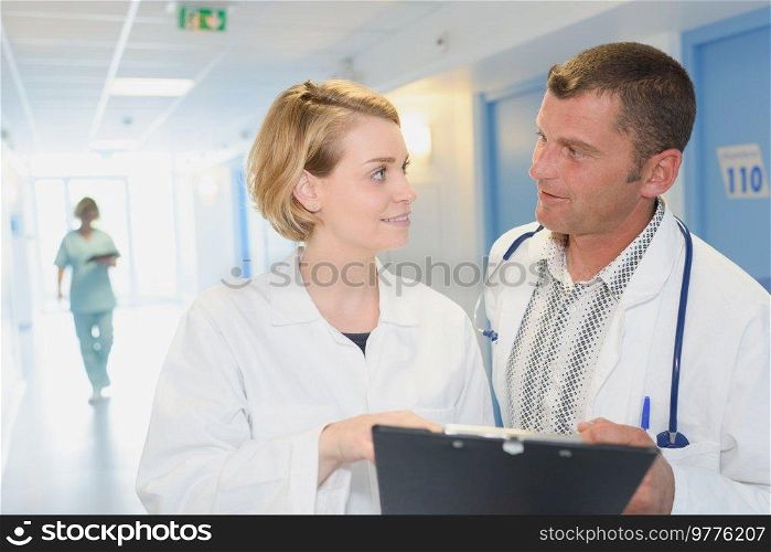 smiling doctors with clipboard walking along hospital corridor